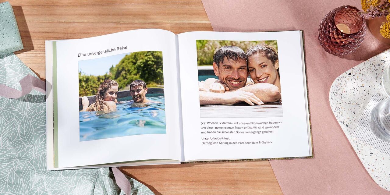 Auf einem Tisch liegt ein aufgeschlagenes CEWE FOTOBUCH. Auf beiden Seiten sind Fotos eines Paares in einem Pool zu sehen. Links steht die Überschrift „Eine unvergessliche Reise“.