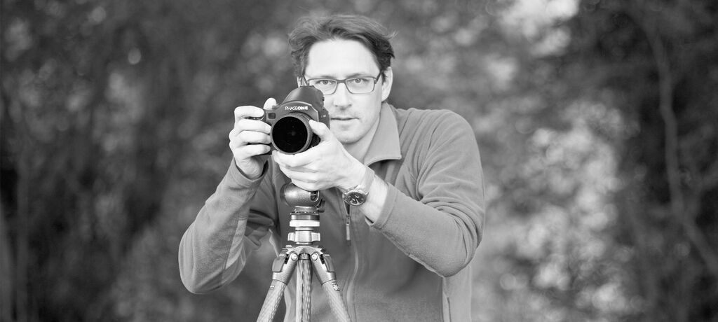 Ein Fotograf hält eine Kamera und steht an einem Stativ.