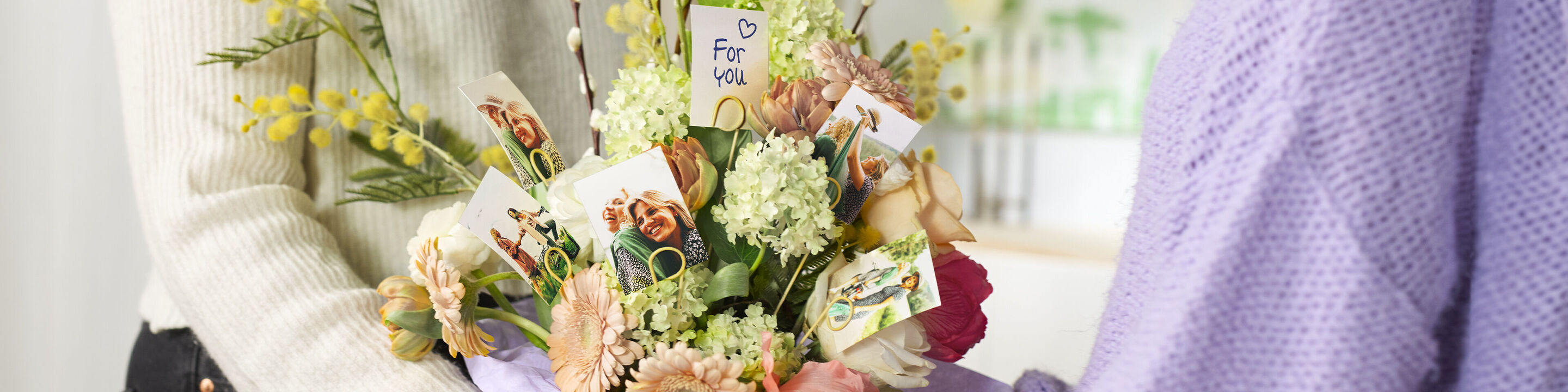 Eine Person überreicht einen bunten Blumenstrauß mit kleinen Karten, die liebe Botschaften zeigen.
