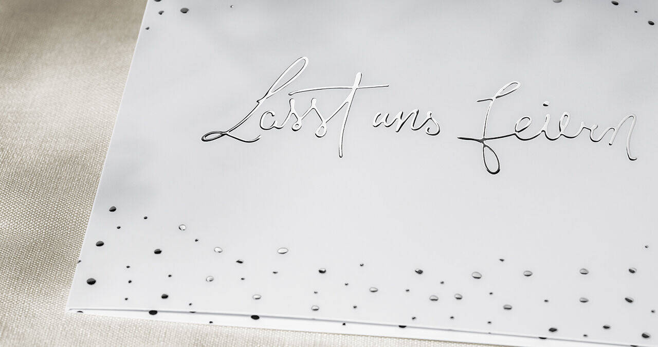 Elegante Grußkarte mit der Aufschrift 'Lasst uns feiern' in geschwungener Schrift, verziert mit kleinen Punkten.