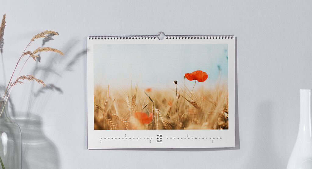 Ein schöner Wandkalender mit einem Bild von Mohnblumen in einem Kornfeld, der an einer Wand hängt