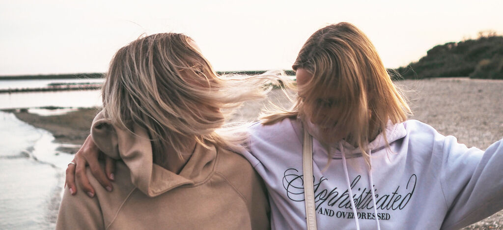 Zwei Frauen umarmen sich am Strand mit wehenden Haaren