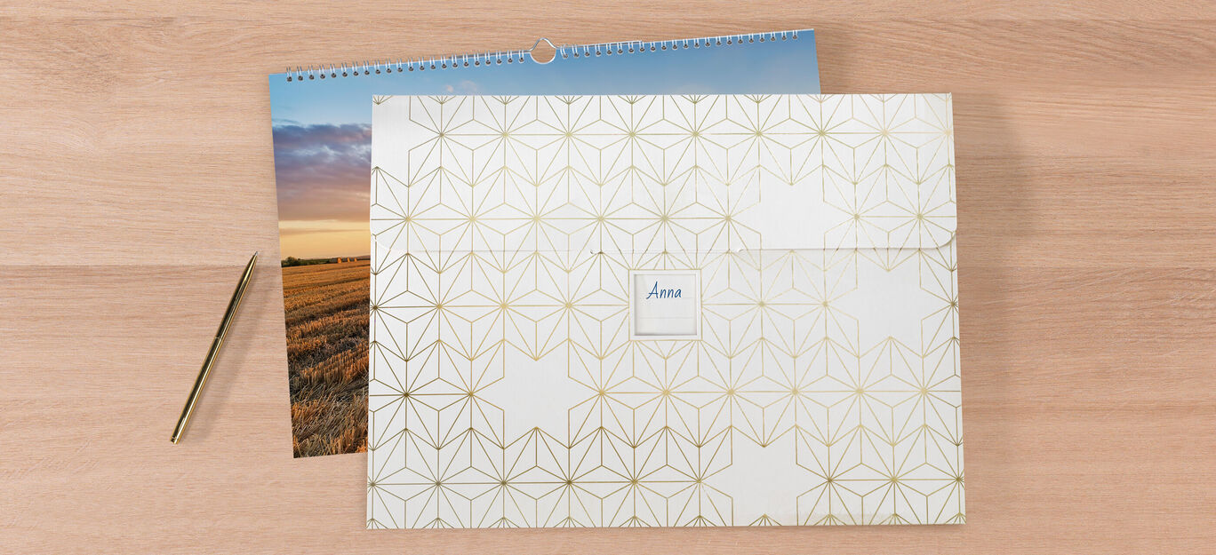 Ein dekorativer Umschlag mit goldenen geometrischen Mustern, daneben ein Kalender mit einem Landschaftsbild.
