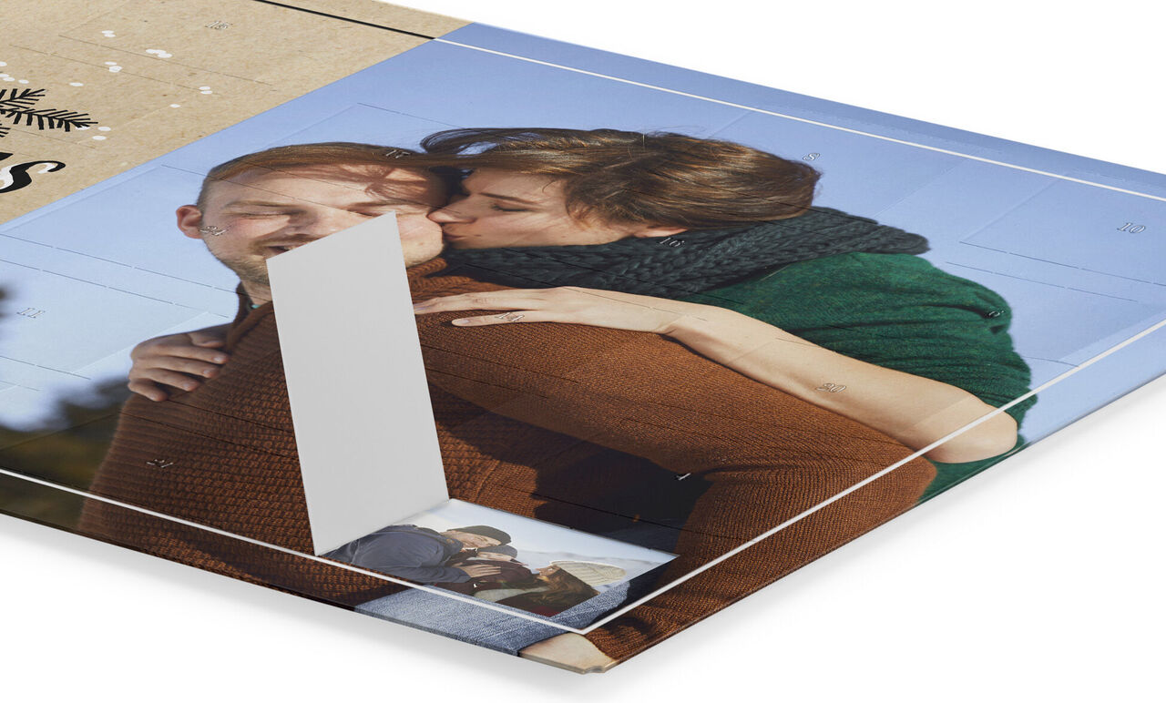 Eine Frau umarmt einen Mann von hinten und küsst ihn auf die Wange. Der Hintergrund zeigt ein CEWE FOTOBUCH mit Bildern, die Erinnerungen festhalten.