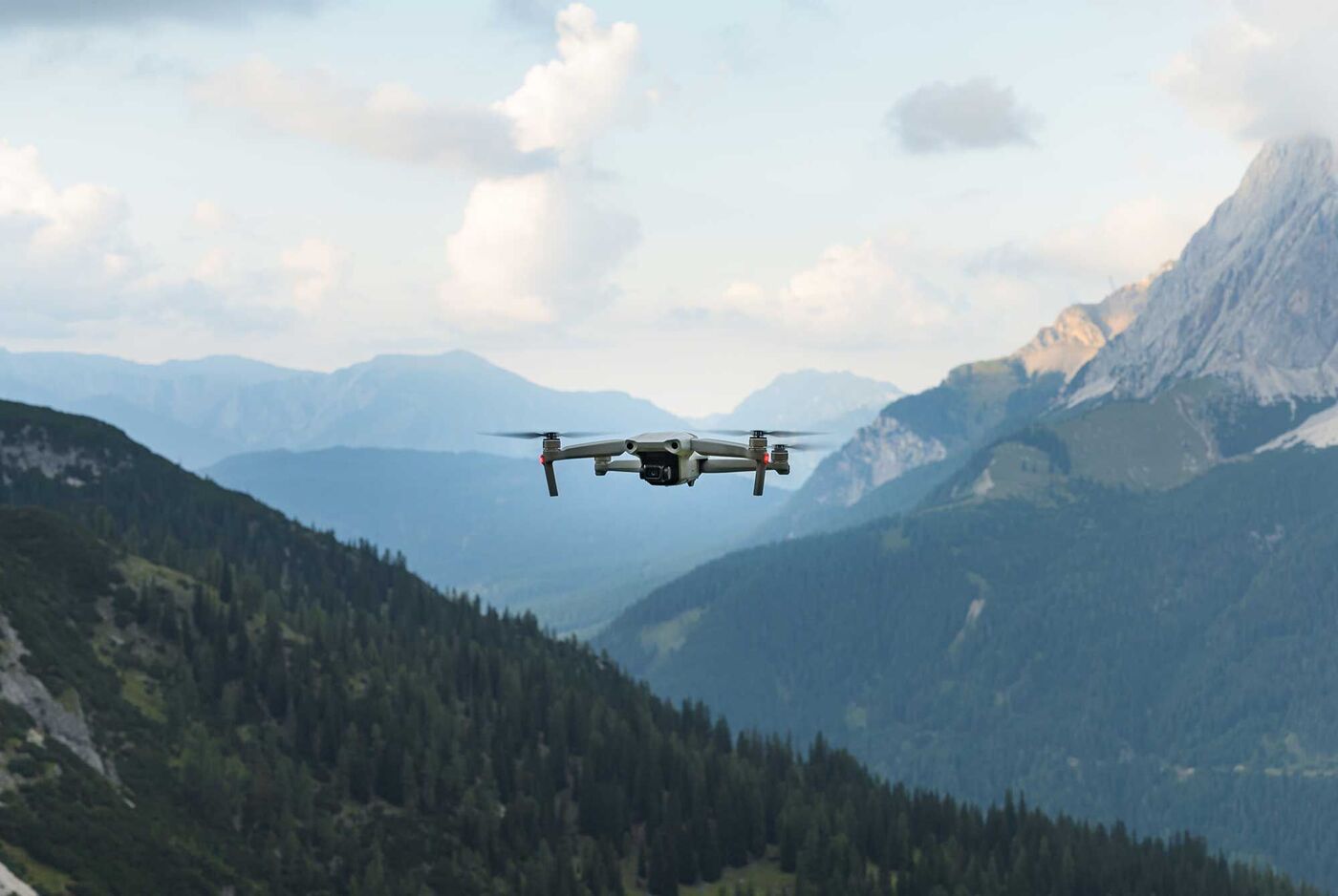 Ein Drohne fliegt hoch über einer bewaldeten Berglandschaft im Tirol.
