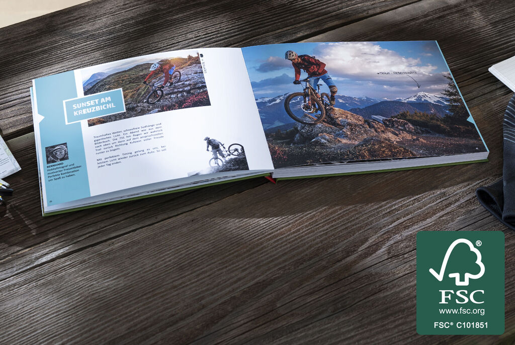 Ein offenes CEWE FOTOBUCH zeigt Bilder von einem Mountainbiker in den Bergen. Auf der linken Seite sind erklärende Texte zu sehen.