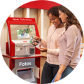 Zwei Frauen schauen sich Fotos an, die sie am CEWE Sofortfotoautomaten drucken lassen.