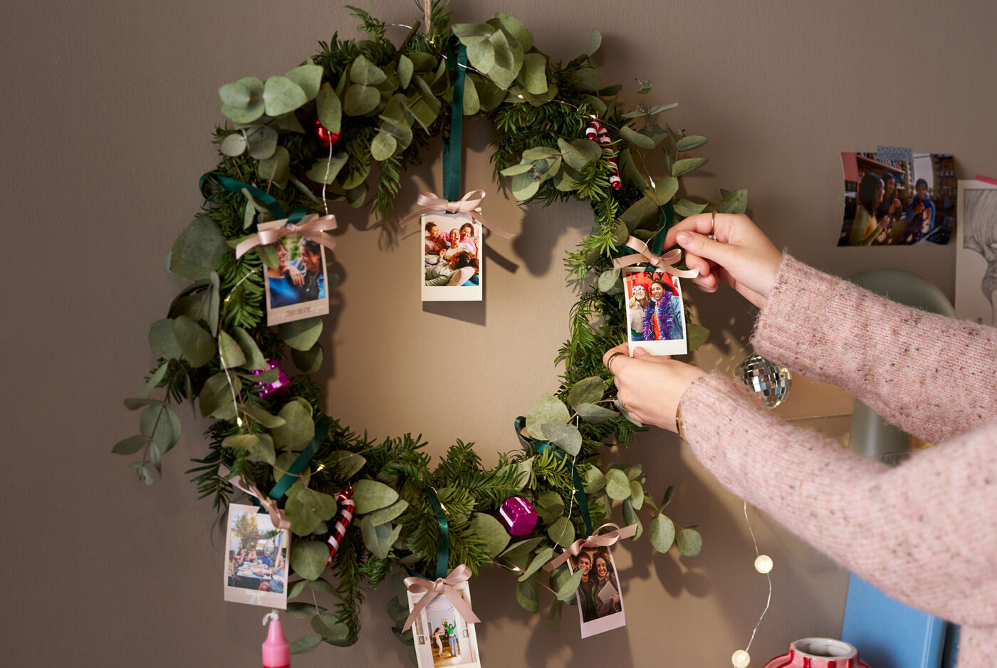 Eine Frau dekoriert mit Fotoanhängern einen weihnachtlich geschmückten Kranz, der an einer Wand hängt.