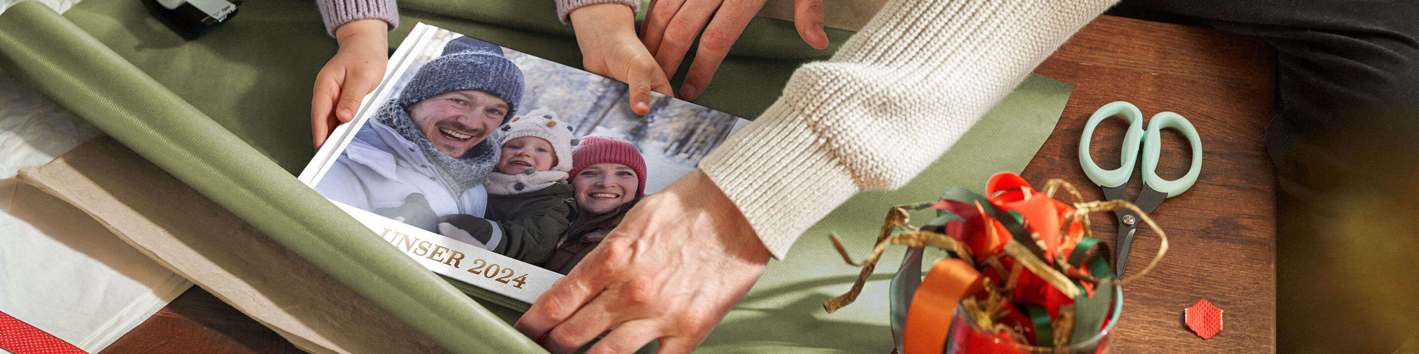 Zwei Personen umarmen ein CEWE Fotobuch auf einem Tisch mit Geschenkpapier und Bastelmateriaal