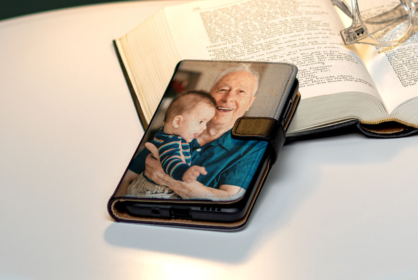 Ein Smartphone-Hülle mit einem Bild eines Babys und einer älteren Person, daneben ein aufgeschlagenes Buch.
