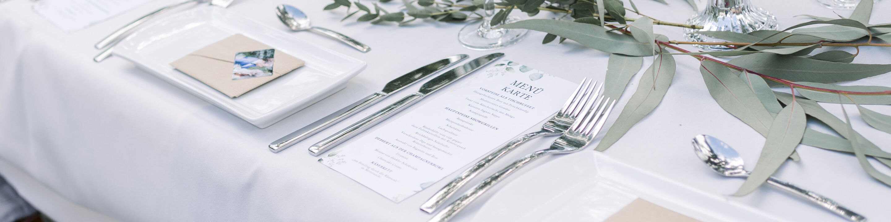 Eleganter Tisch mit Besteck, Menü und grünem Dekor
