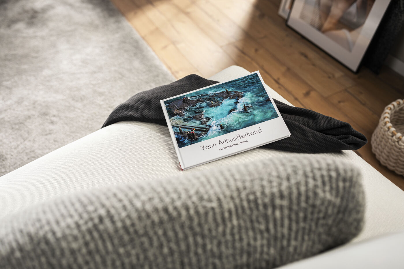 Ein CEWE FOTOBUCH liegt auf einer Couch mit einer grauen Decke und einem grauen Kissen.