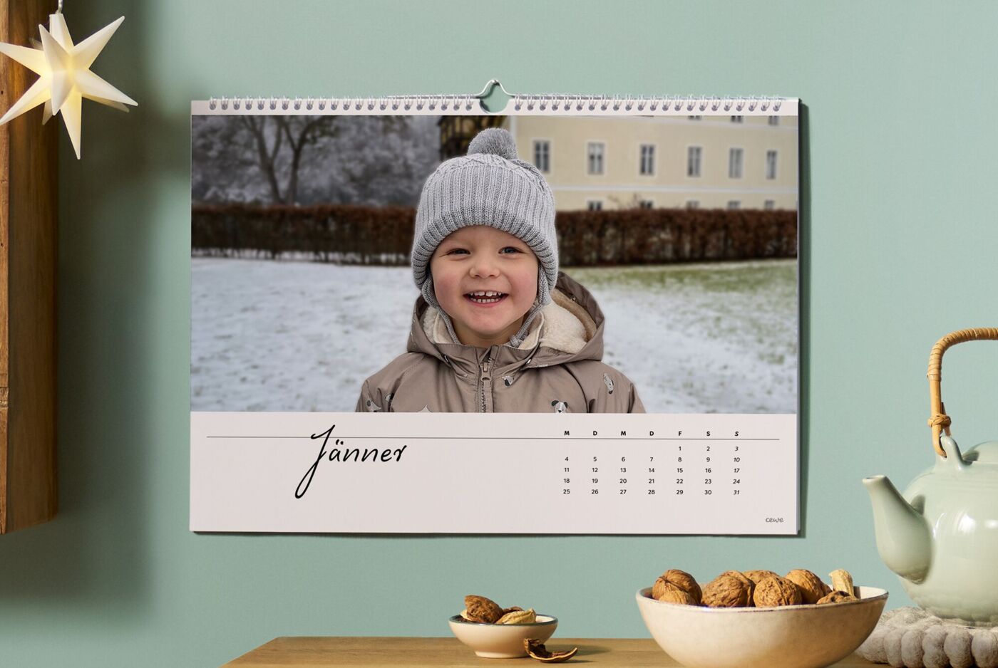 Ein fröhliches Kind mit einer Mütze im Schnee lächelt vor einem Wandkalender.