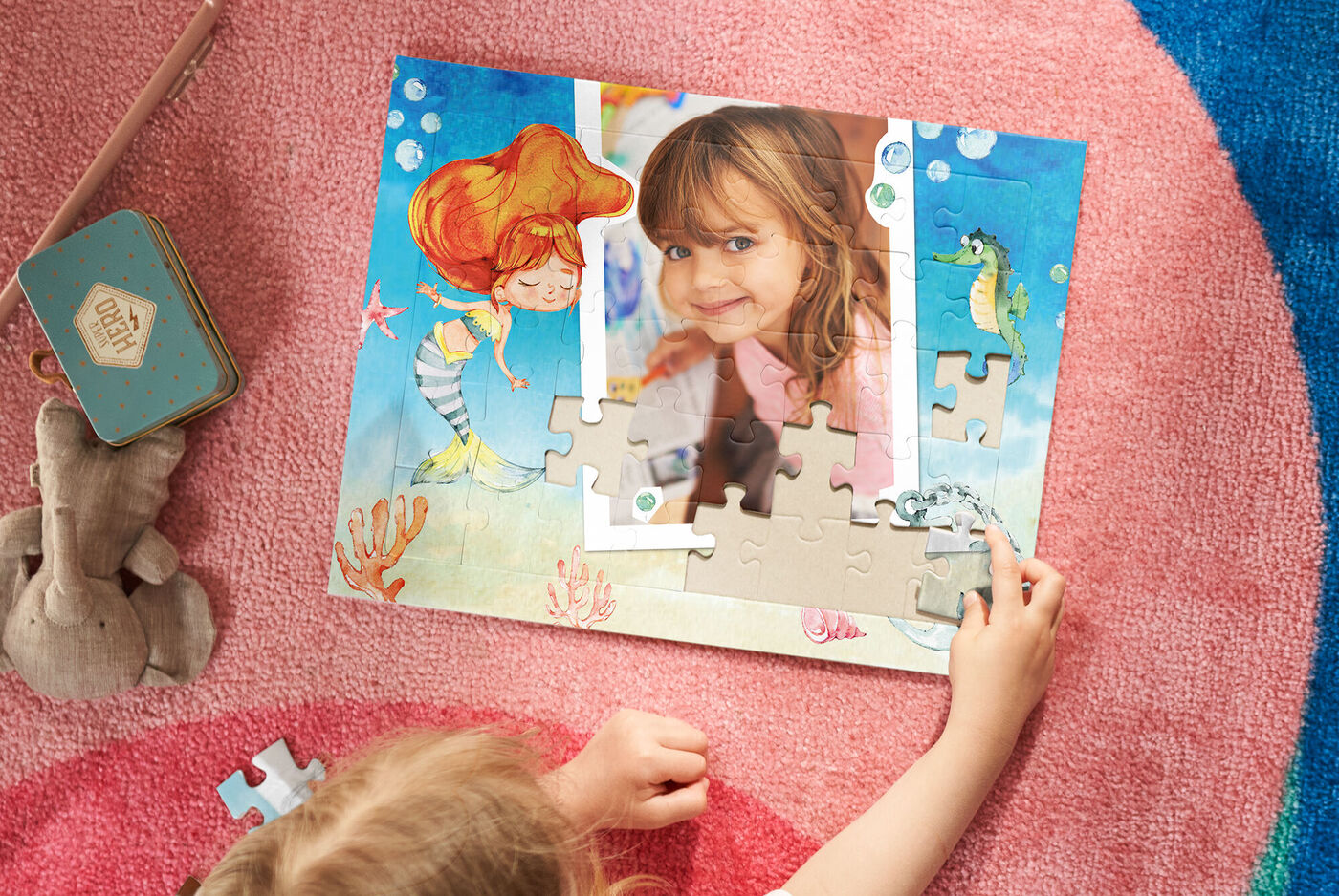 Ein Kind spielt mit einem Puzzle, um ein Foto zu gestalten. Der Puzzle-Hintergrund ist maritim mit einem Seepferdchen und bunten Fischen.