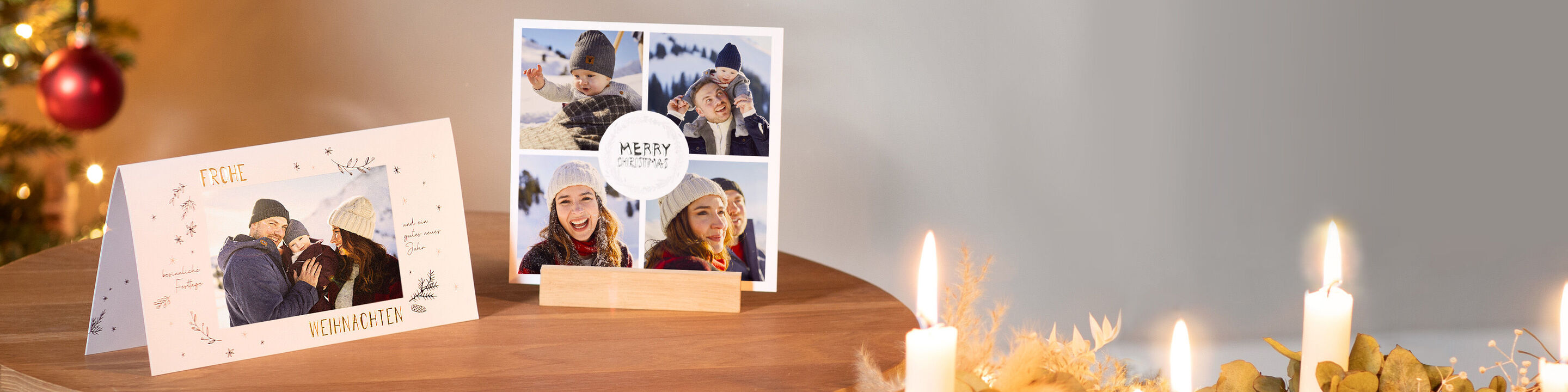 Zwei Weihnachtskarten von CEWE auf einem Tisch mit Adventkranz im Vordergrund. Die Karte links als Klappkarte und quadratische Grußkarte.