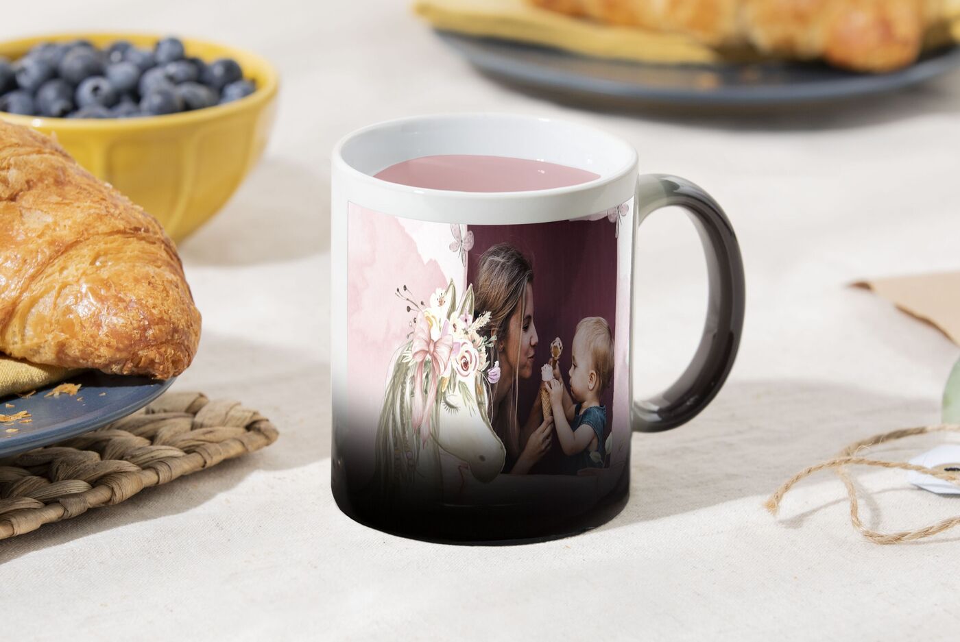 Tasse mit einem Bild einer Mutter, die mit ihrem Baby spricht, umgeben von Gebäck und Blaubeeren