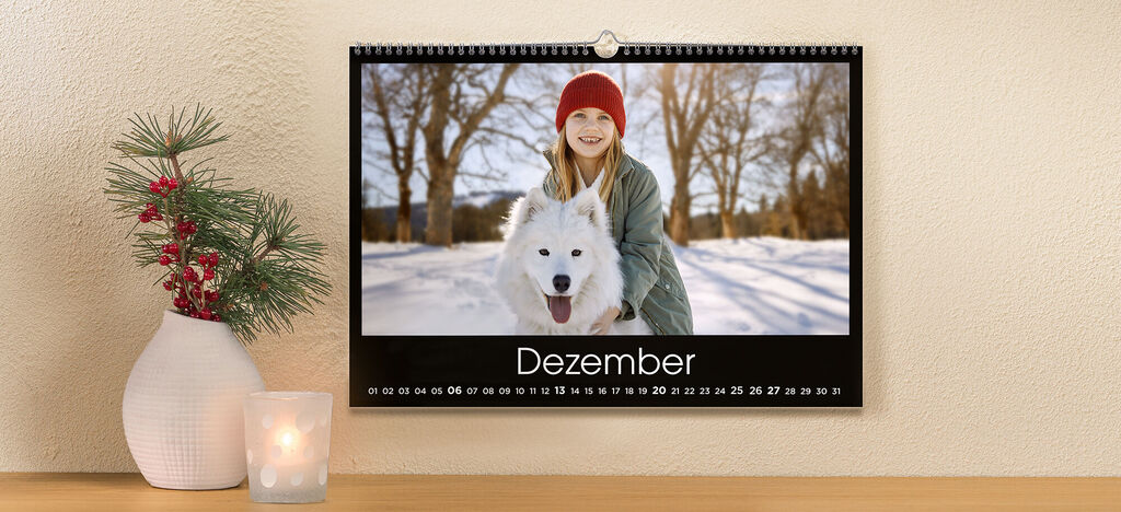 Eine persönliche Dezember-Seite des CEWE Fotokalenders mit einer Person und einem weißen Hund im Schnee.