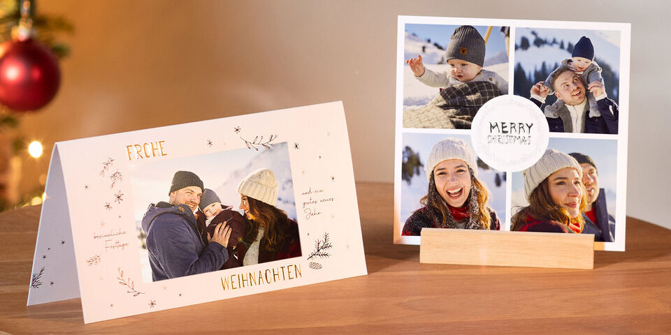 Zwei Weihnachtskarten von CEWE auf einem Tisch mit Adventkranz im Vordergrund. Die Karte links als Klappkarte und quadratische Grußkarte.