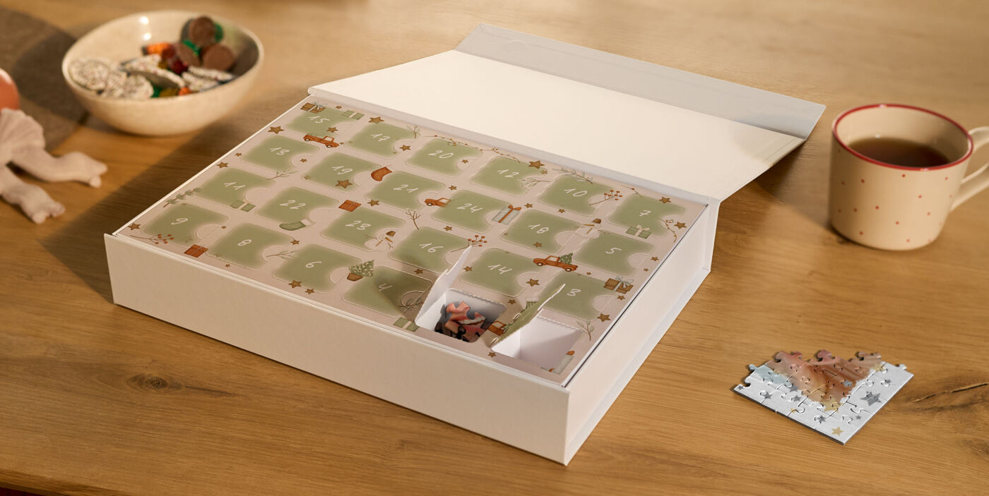 Premium Puzzle-Adventskalender mit zwei geöffneten Türchen und einem bereits gepuzzelten Puzzlestück in weihnachtlicher Umgebung