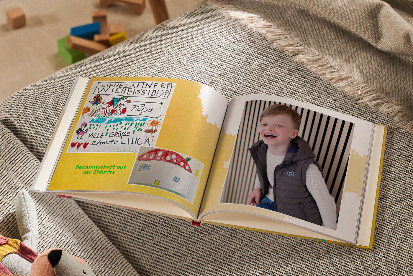 Offenes Fotobuch mit bunten Zeichnungen von Kindern auf einer Seite und einem Kind auf der anderen Seite.