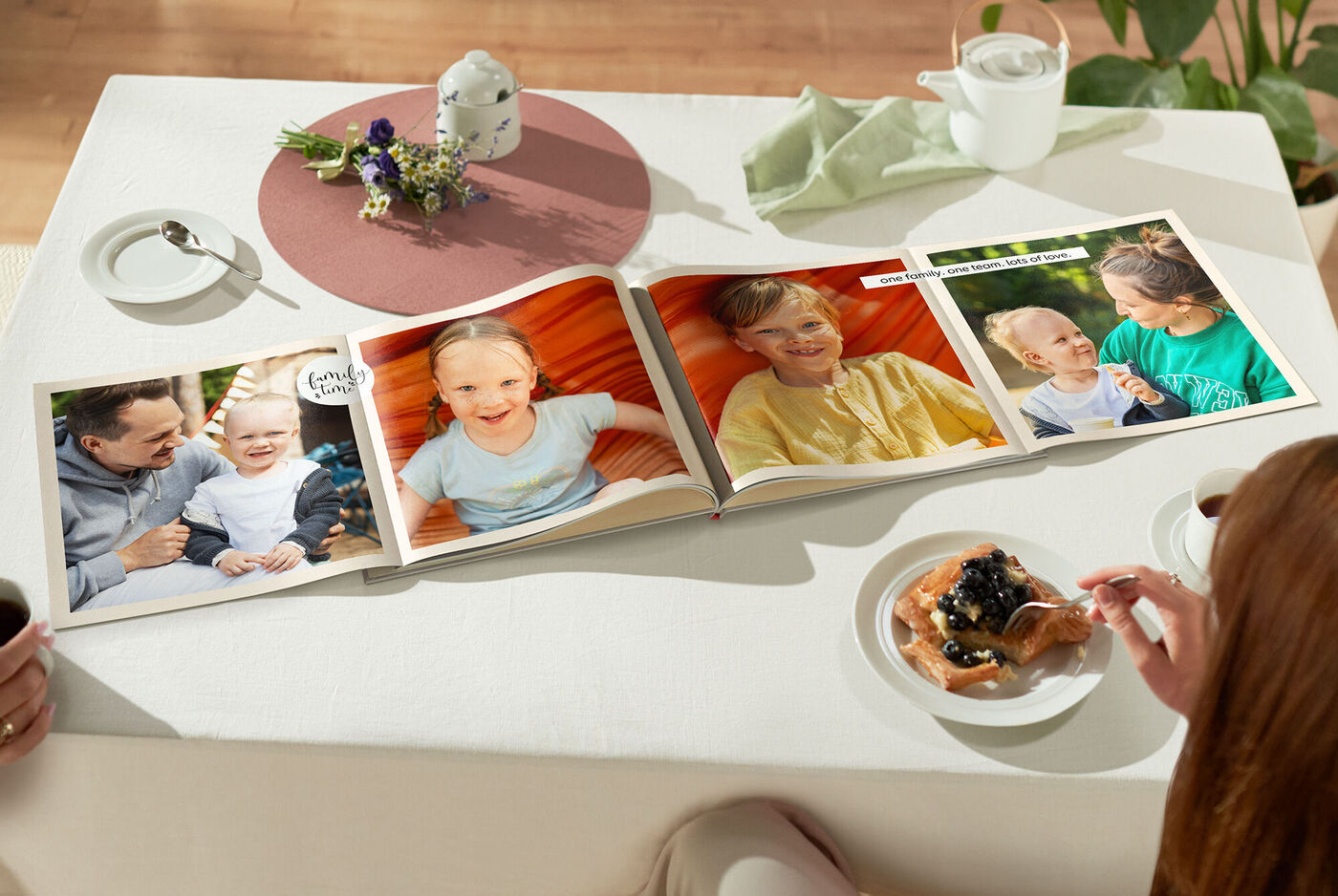 Ein offenes CEWE FOTOBUCH liegt auf einem Tisch neben einer Tasse Kaffee und einem Dessert. Es zeigt verschiedene Fotos von glücklichen Momenten mit Freunden oder Familie, die Freude und gemeinsames Erleben widerspiegeln