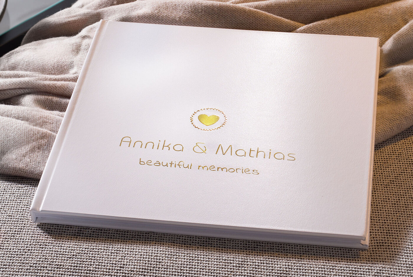 Ein weißes Fotobuch mit goldener Schrift. Darauf stehen die Namen Annika und Mathias sowie der Text „beautiful memories”.