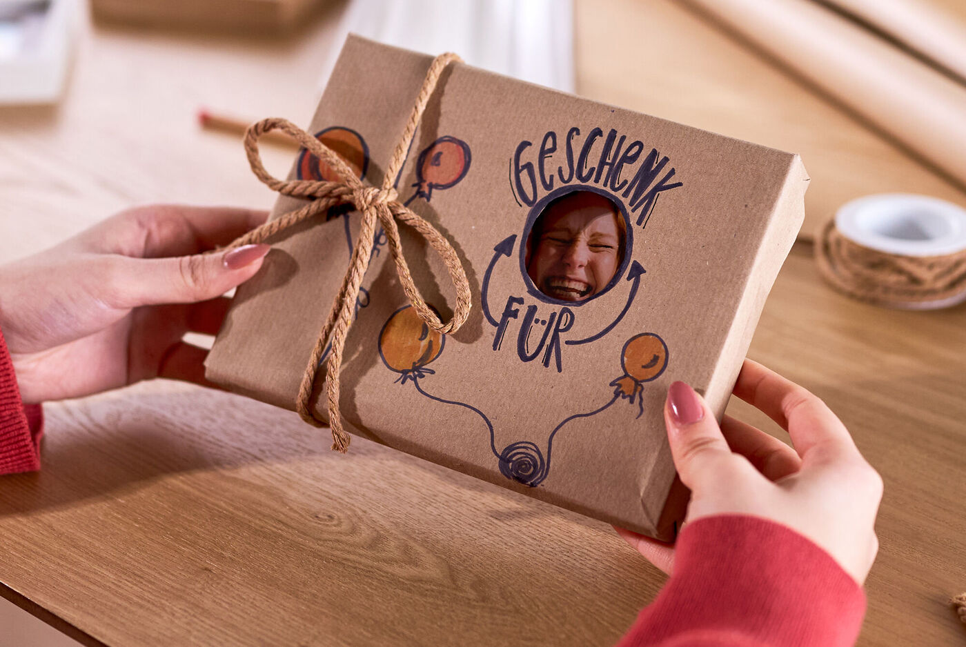 Eine Frau hält ein verpacktes Geschenk in den Händen. Eine Aussparung im Geschenkpapier zeigt einen Teil des Foto dahinter.