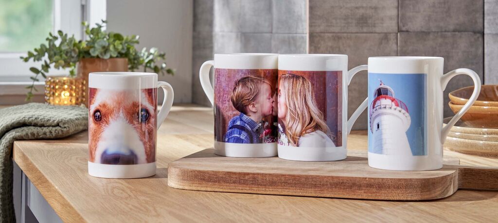 Drei Tassen mit individuellen Fotos auf einem Holzbrett, umgeben von einer pflanzlichen Dekoration