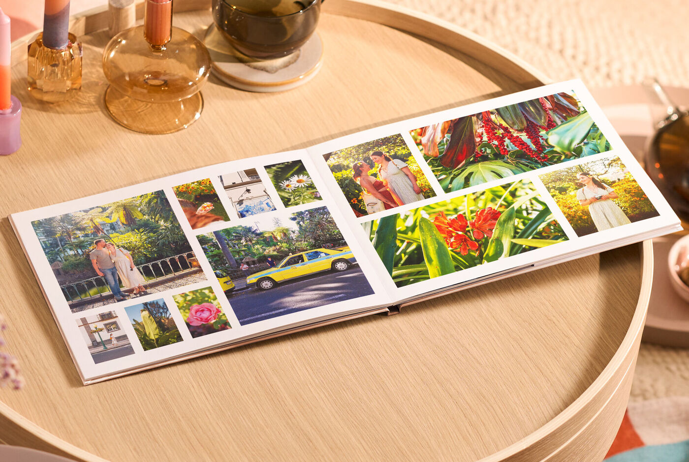 Offenes CEWE FOTOBUCH auf rundem Holztisch mit vielen bunten Reisefotos in verschiedenen Größen.