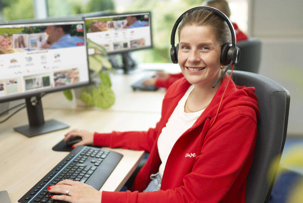 Eine Mitarbeiterin von CEWE arbeitet am Computer mit Headset, um Kunden zu unterstützen