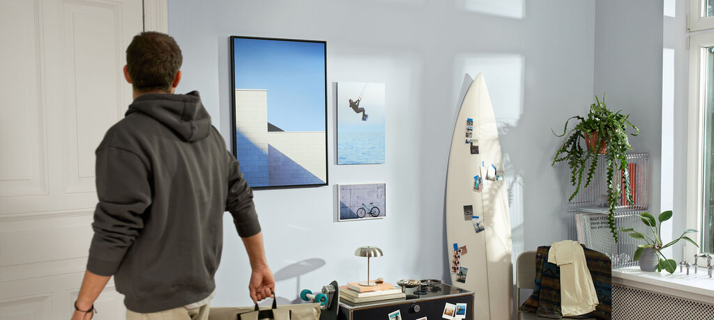Junger Mann betritt einen Raum mit surfbrett und Bildern an der Wand.